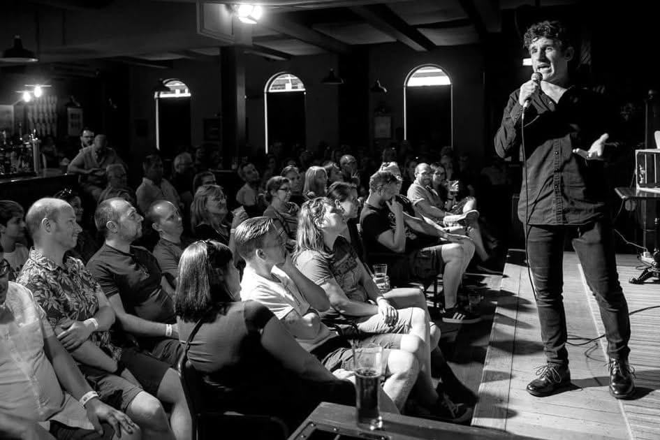 Side-on photograph of a stand-up comedian and seated audience at The Charles Bradlaugh